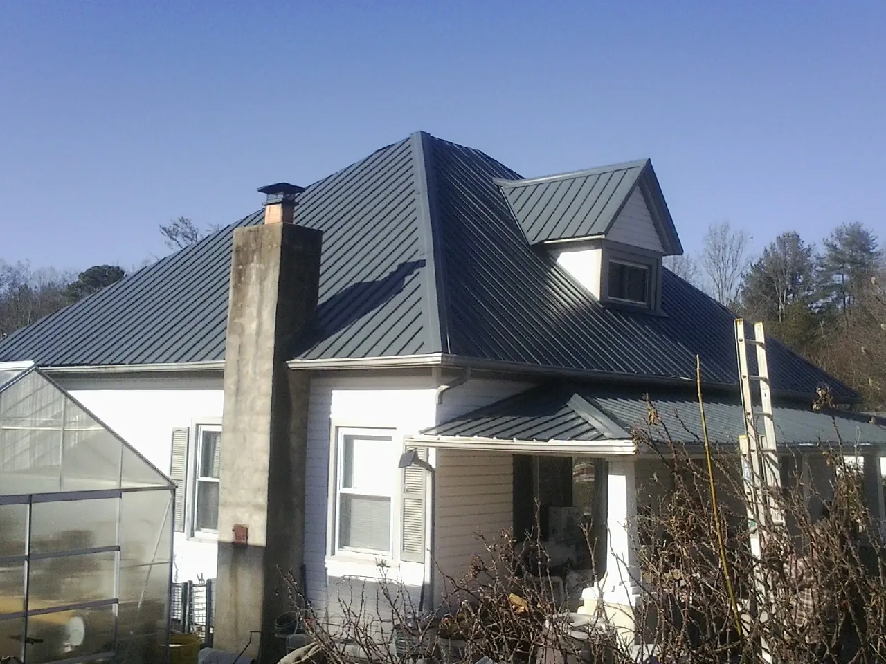 Dark blue standing seam metal roof on a white farmhouse with dormer — Slate & Tile Roof Repair by Roofing Brothers in Keyesport