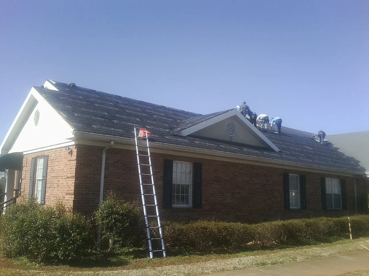 Crew tearing shingles off a brick ranch roof with a ladder set — Emergency Roof Repair work by our crew in Keyesport