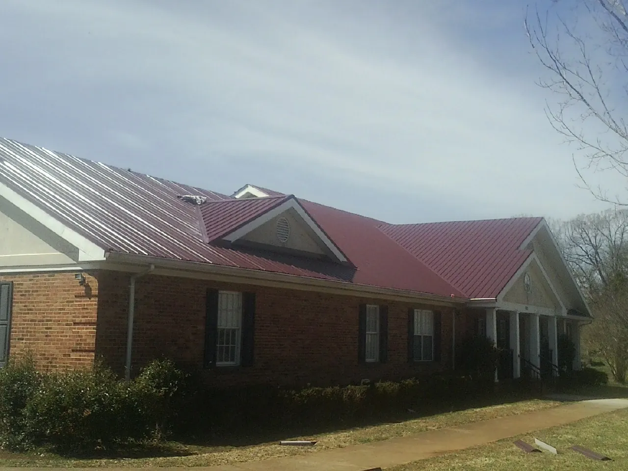 Red metal roof with gabled entries on a long brick building, from a Hail Damage Roof Repair job in Keyesport