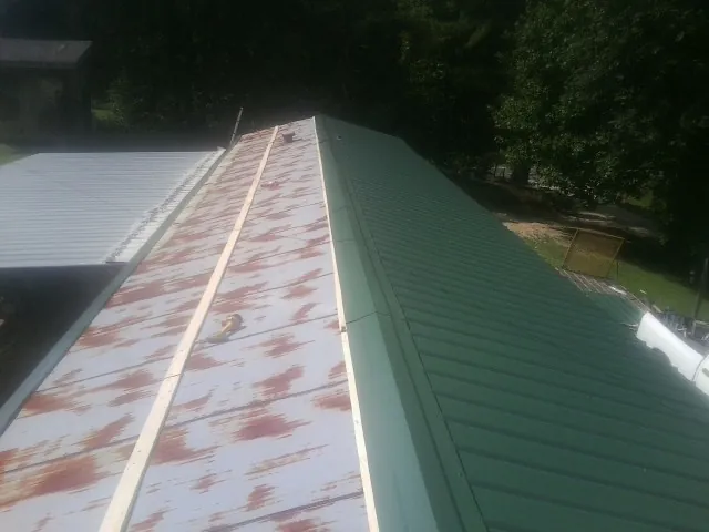 Old rusted panels beside newly installed green metal roofing — Wind Damage Roof Repair by Roofing Brothers in Keyesport