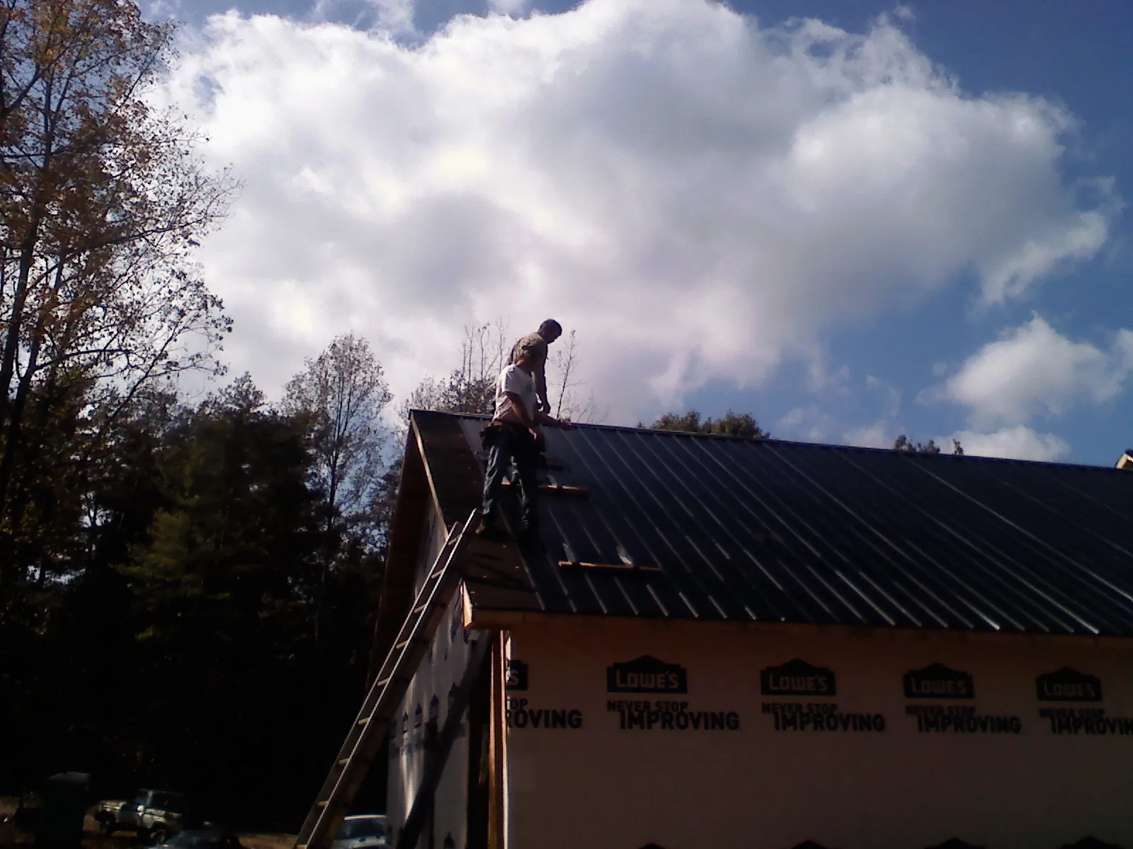 Roofer fastening dark metal panels high against a cloudy sky, from a Roof Inspection job in Keyesport