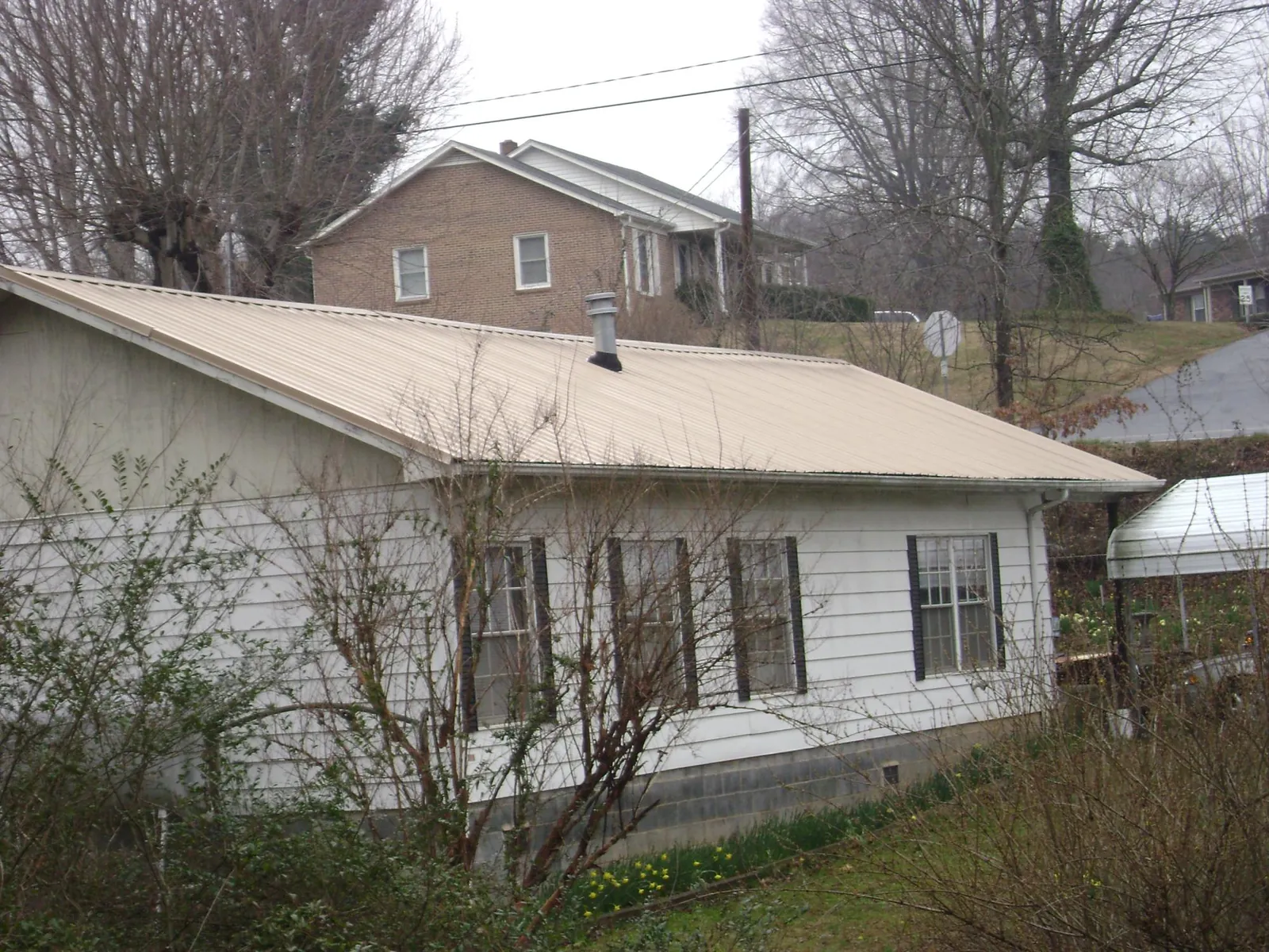Tan metal roof on a white sided house set into a hillside — Commercial Roofing by Roofing Brothers in Keyesport